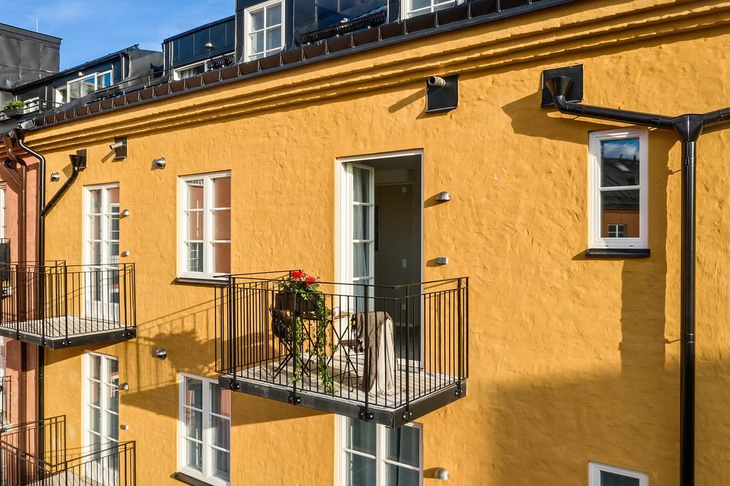 Närbild på den gula putsade fasaden med utanpåliggande balkonger, smidesräcken och vita spröjsade fönster.